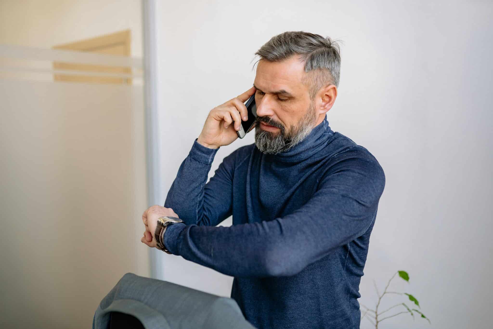 a man looking at his watch while talking on the phone